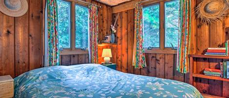 Un dormitorio de cabaña de madera con cama, ventanas y una estantería.