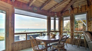 A wooden cabin with a round dining table and chairs, large windows overlooking the ocean, and a colorful rug on the floor. - Lakefront Montague Cottage w/ Deck & Beach! (Montague)