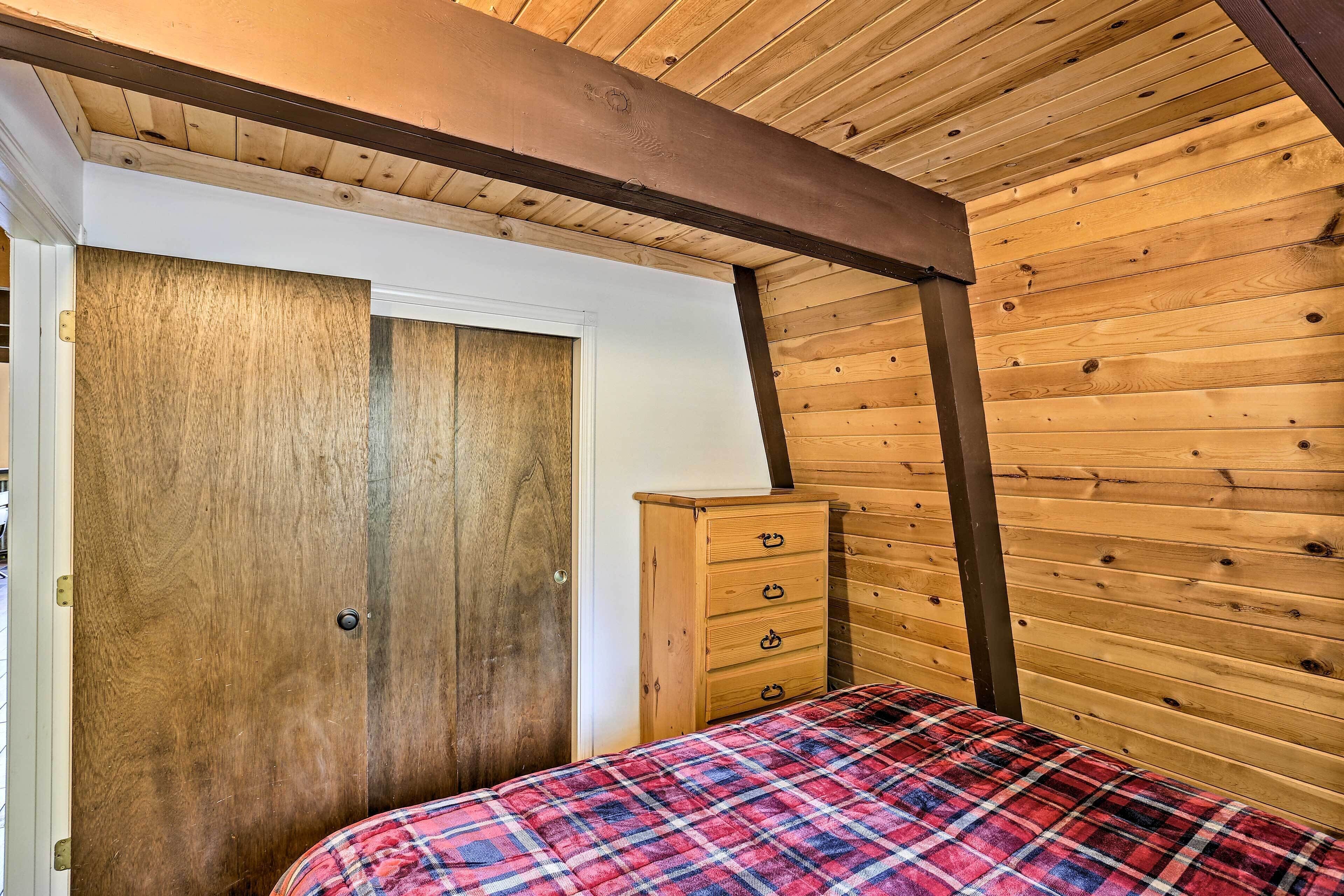 Un dormitorio con techo de madera, colcha escocesa, cómoda de madera y una puerta.