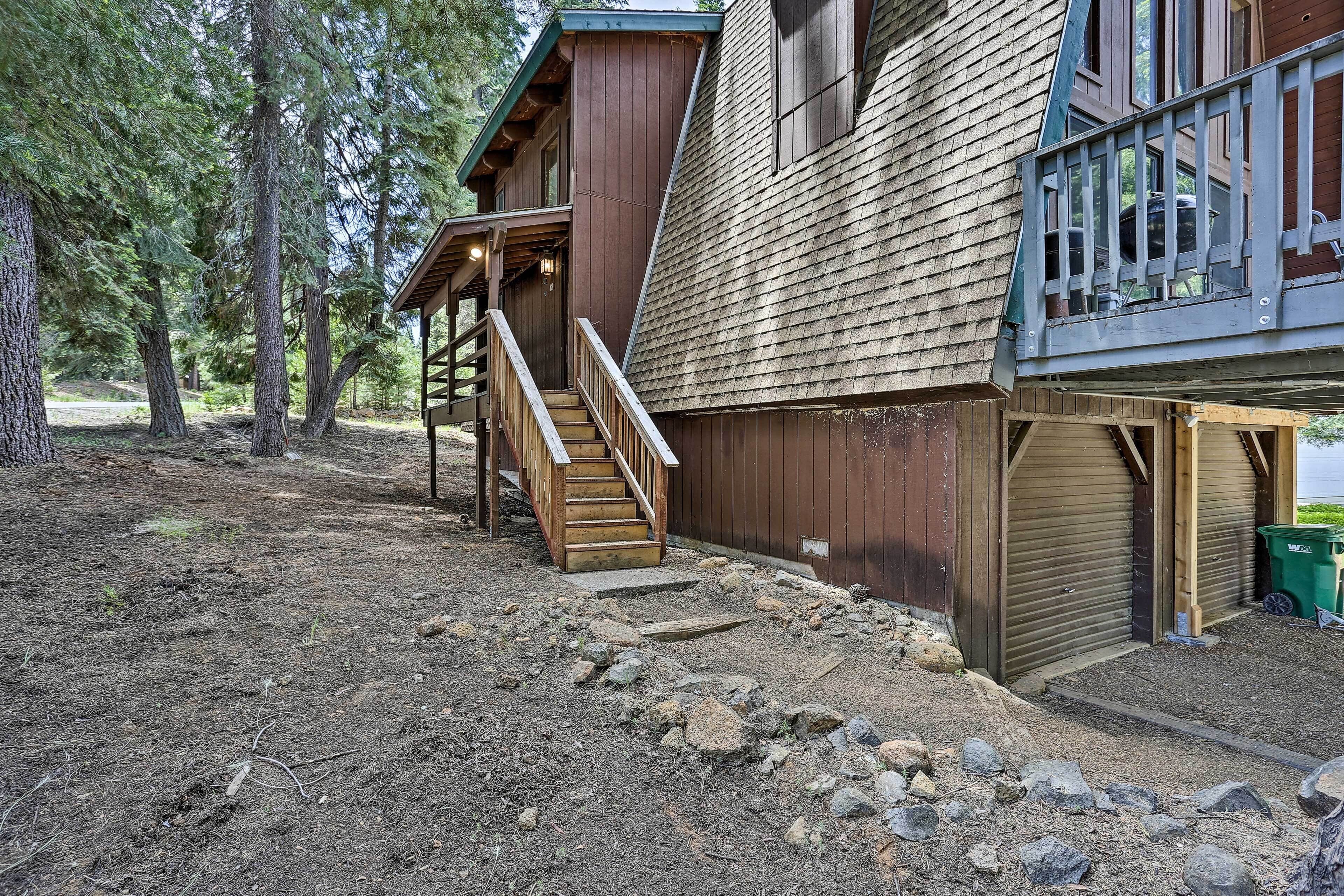 A wooden cabin with a wooden staircase leading to a deck, surrounded by trees.
