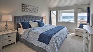 Ein Schlafzimmer mit einem großen Bett, einem Nachttisch, einer Kommode und einem Fenster mit Blick auf das Wasser.