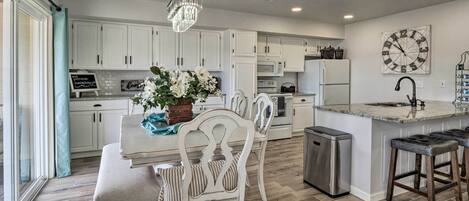 A modern kitchen with white cabinetry, a central island with bar stools, a chandelier, and a clock on the wall.