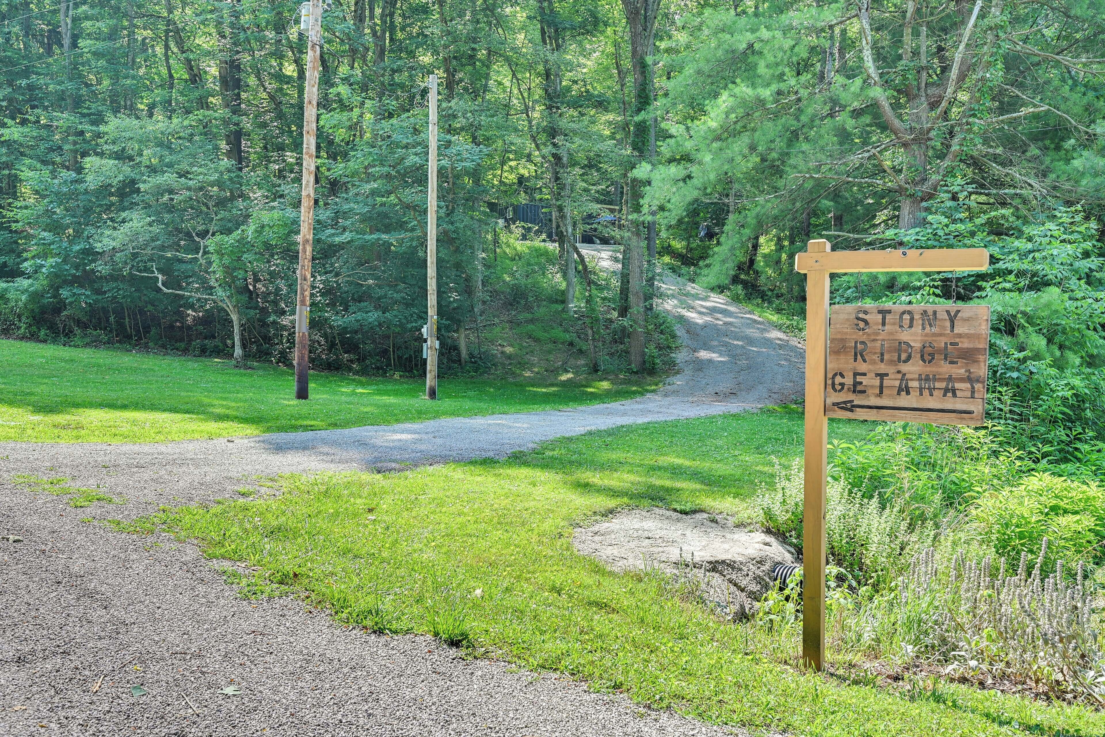 A wooden signpost with 'Stony Ridge Getaway' written on it, set in a wooded area with a gravel path.