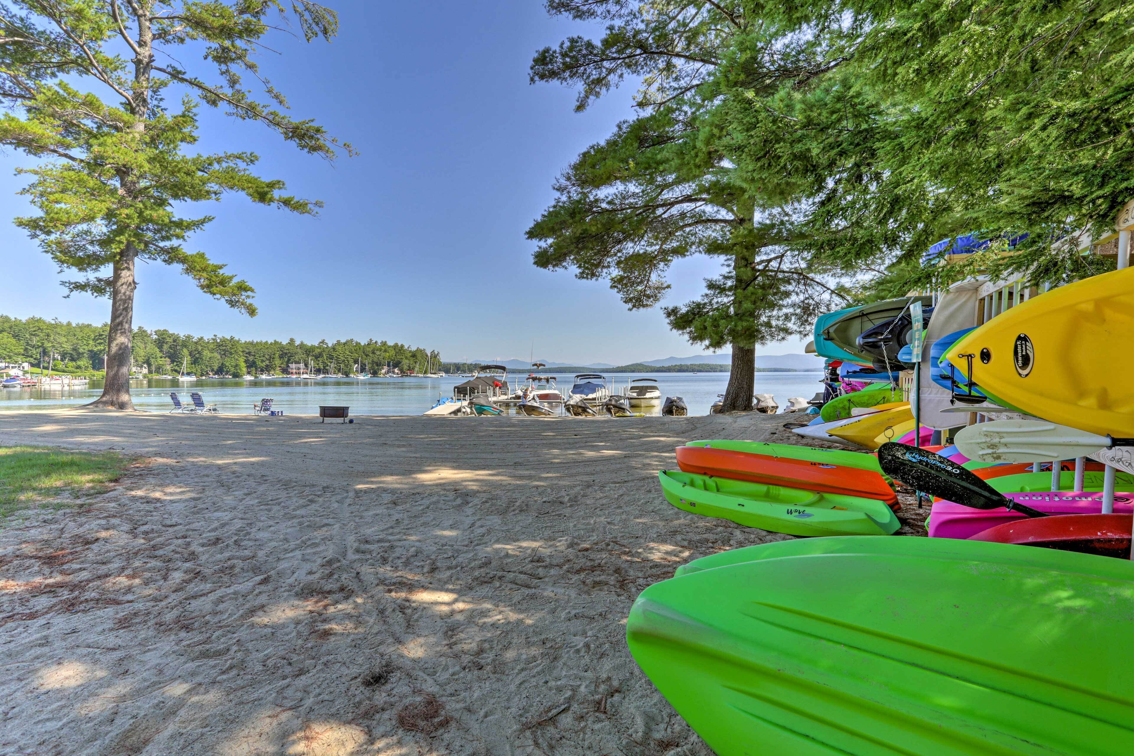 A beach with kayaks lined up and a clear view of the water and distant mountains.