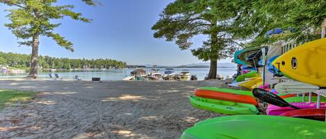 A beach with kayaks lined up and a clear view of the water and distant mountains.