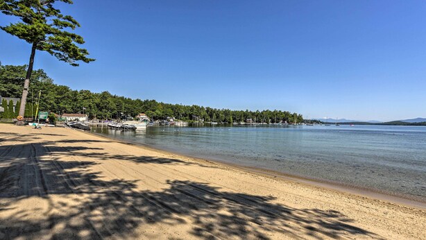 Une plage à l’eau claire, avec un rivage sablonneux et une rangée d’arbres en arrière-plan.
