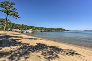 Een strand met helder water, een zandstrand en een rij bomen in de verte.
