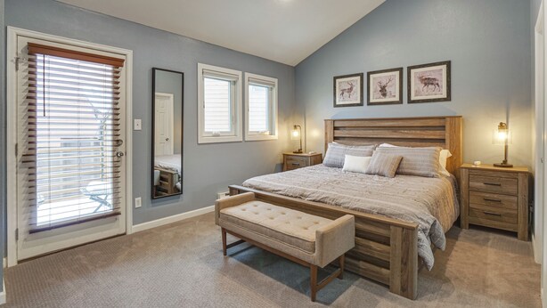 A bedroom with a large bed, a bench, two bedside tables, a mirror, and three framed pictures on the wall.