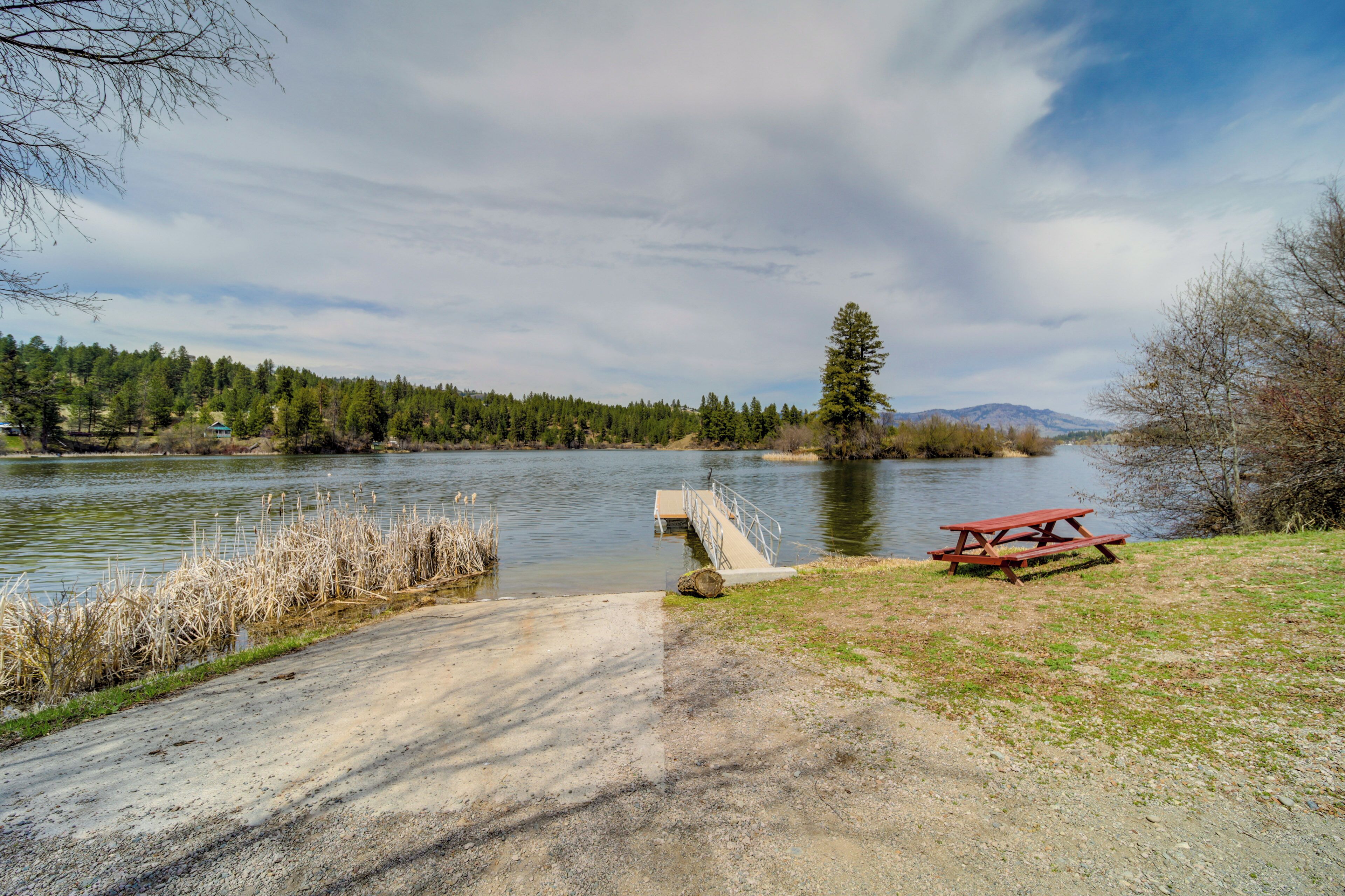 A picnic table by a riverside path with a bridge leading to a small island.
