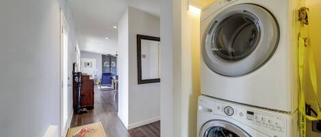 A laundry area with a washing machine and dryer, a hallway with wooden flooring, and a door leading to another room.