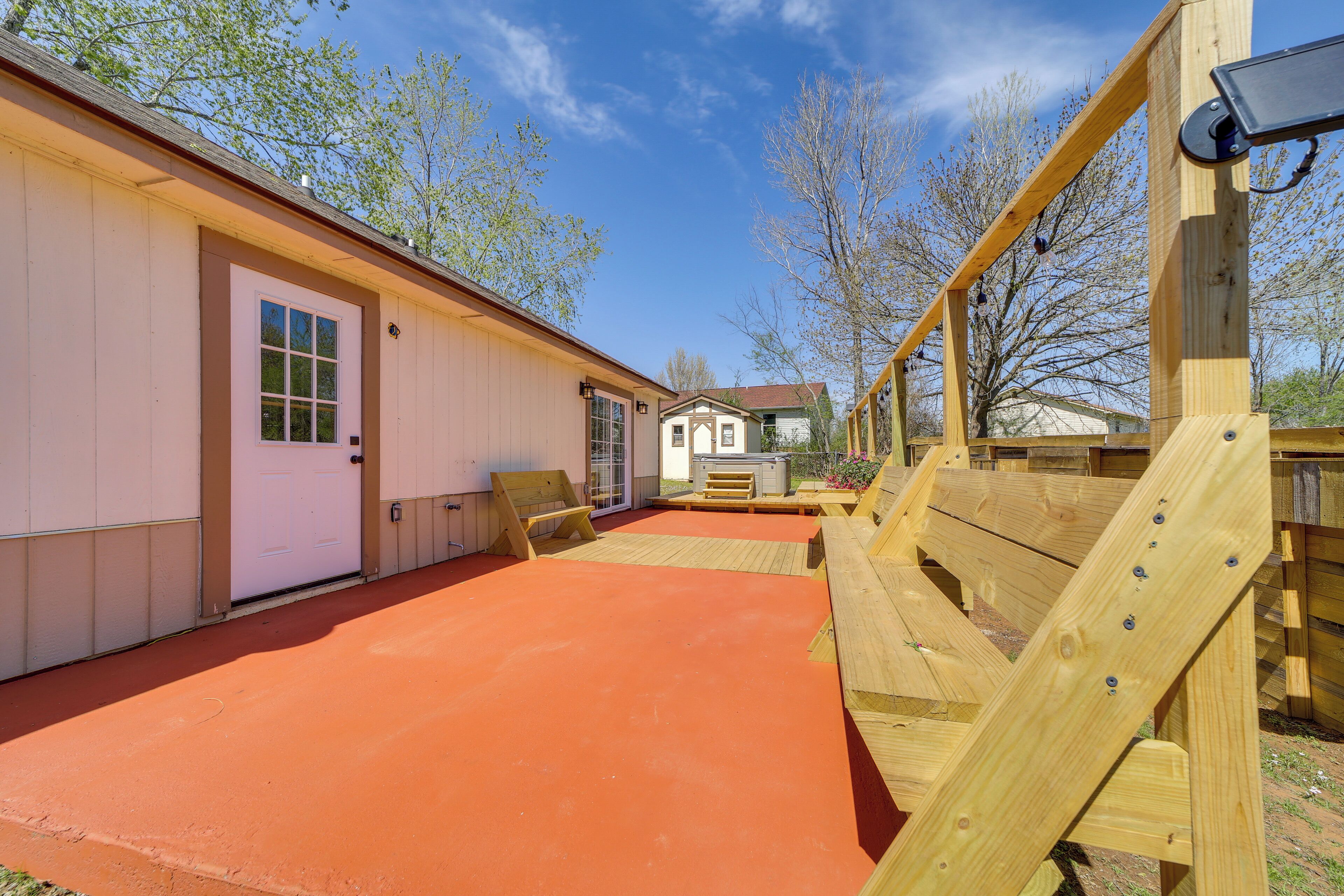 A wooden deck with a red surface, a wooden play structure, and a building with a white door.