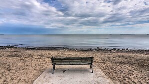 Eine Bank an einem sandigen Strand mit ruhiger See und bewölktem Himmel.