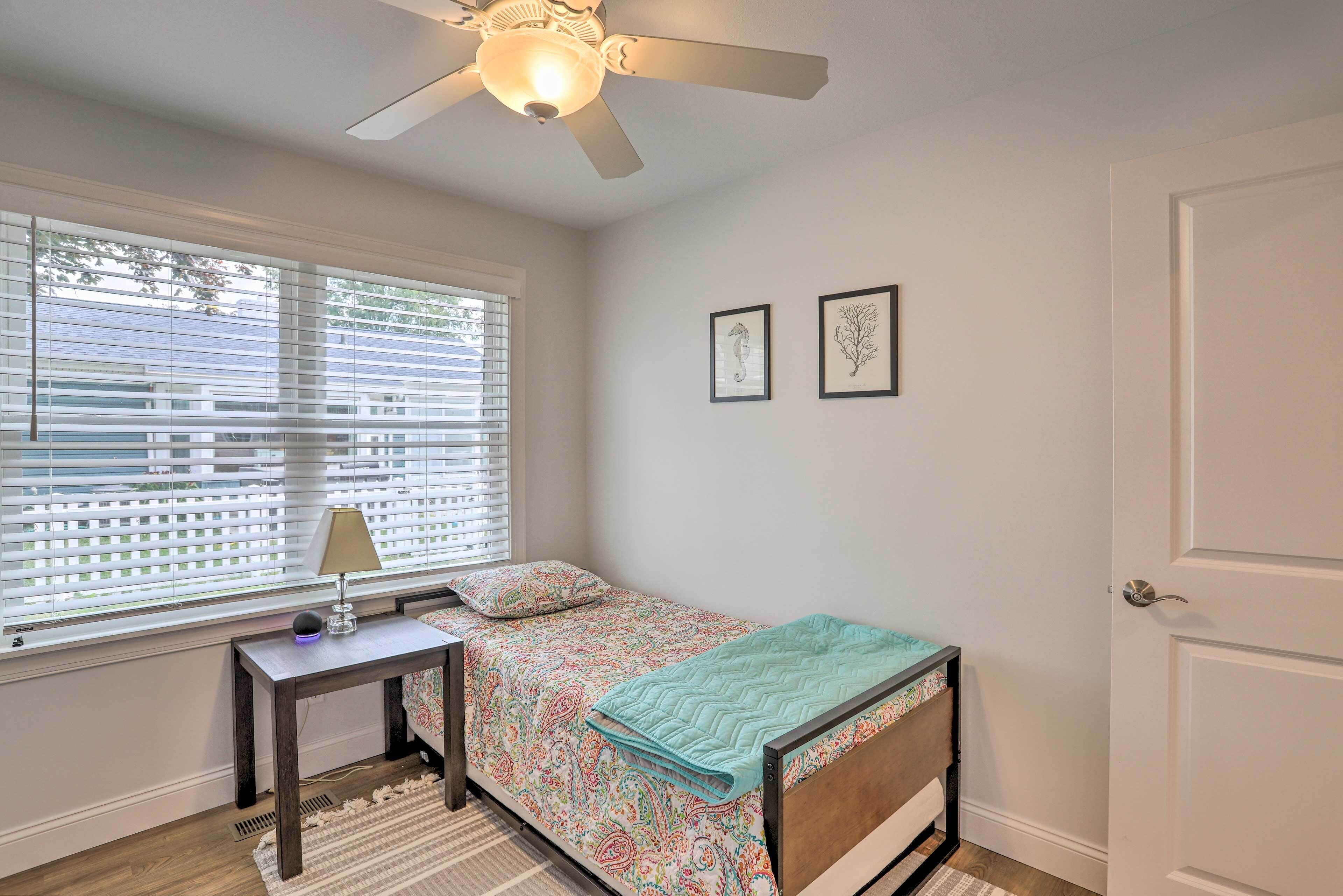 A bedroom with a bed, a nightstand, a lamp, a ceiling fan, and two framed pictures on the wall.