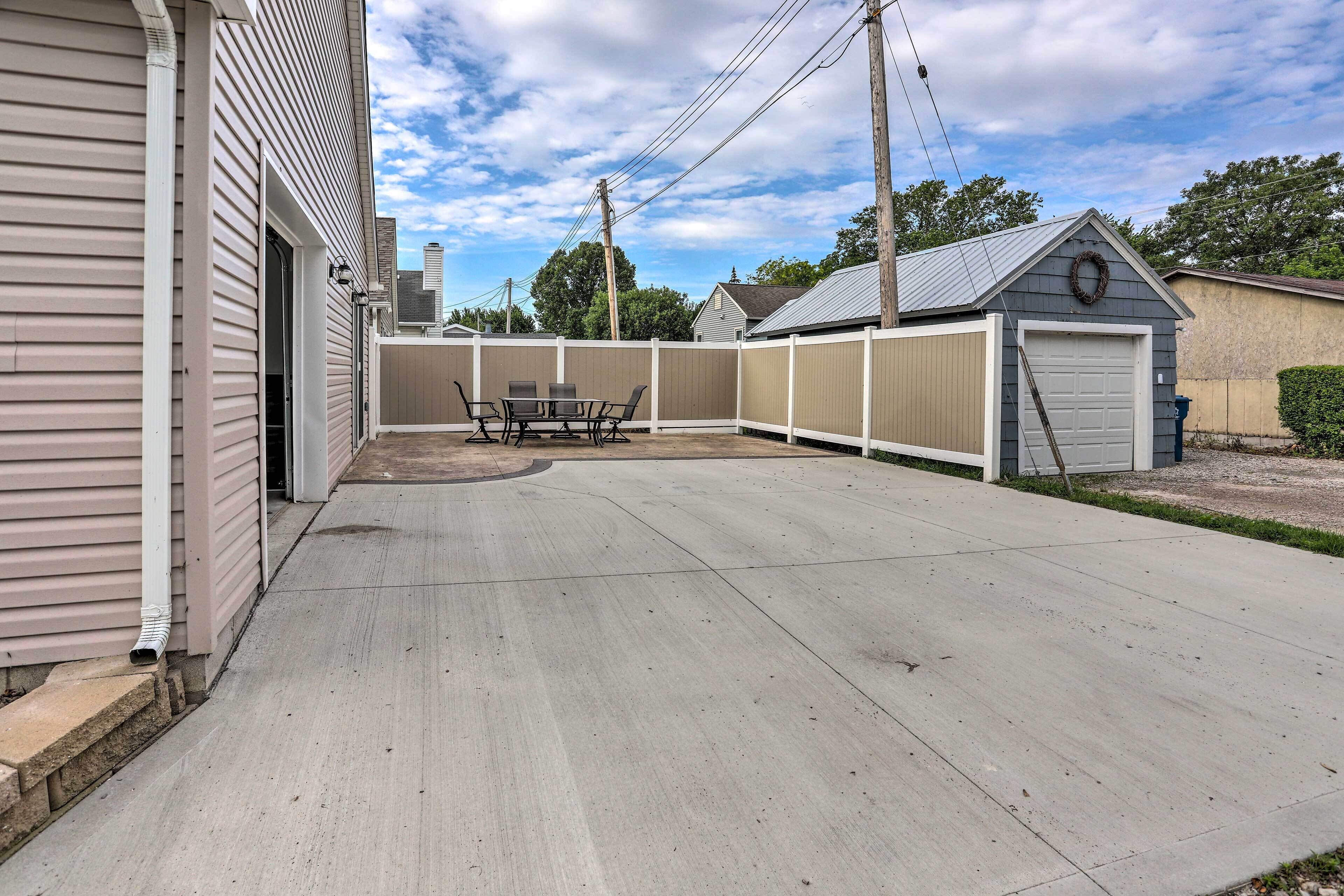 Un patio trasero residencial con un patio de concreto, una mesa y sillas, un garaje y un área cercada.
