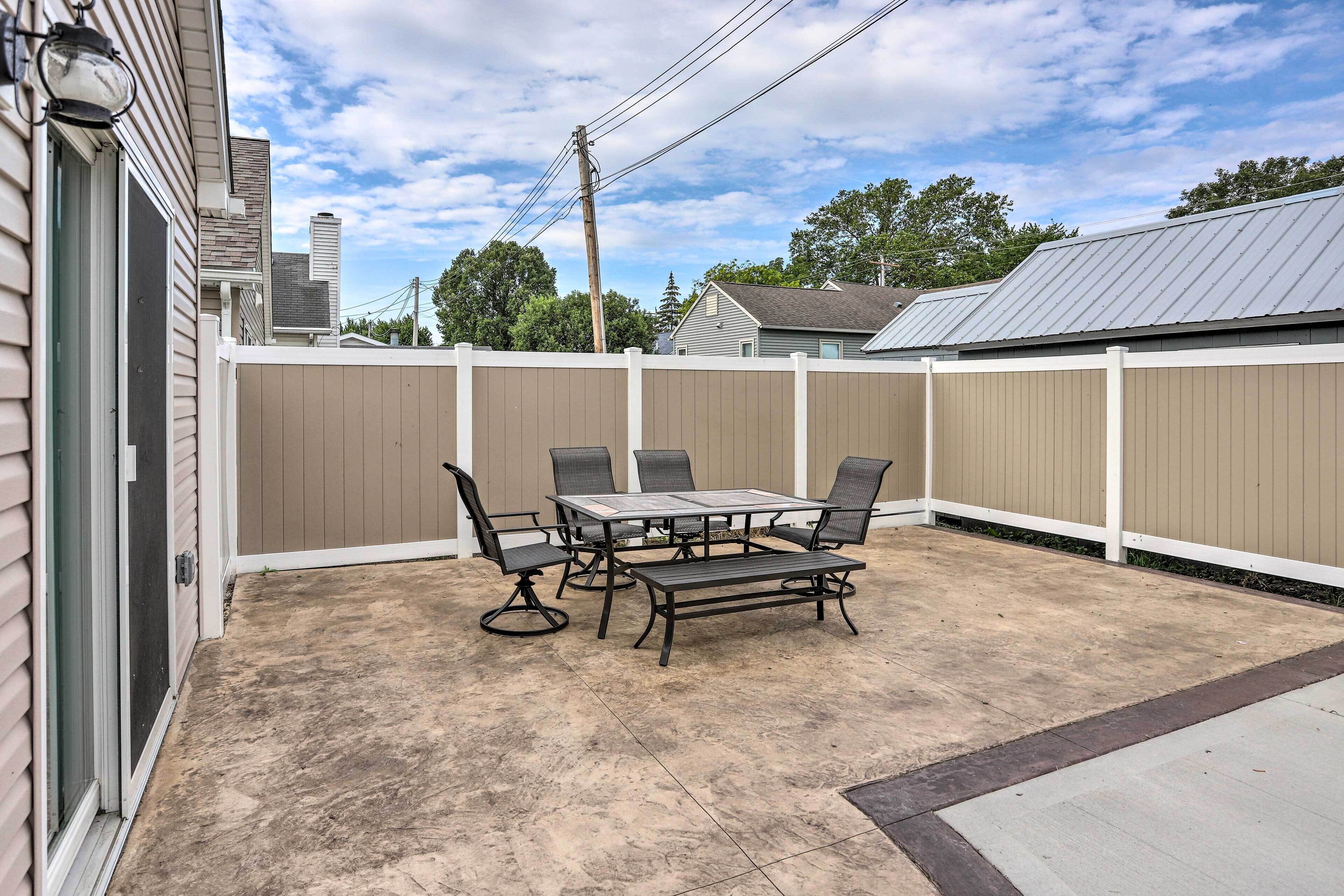 An outdoor patio with a table and chairs, a concrete floor, and a wooden fence.