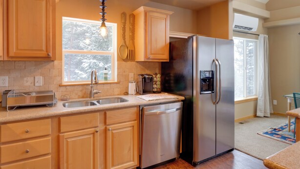 A kitchen with wooden cabinets, stainless steel appliances, a window with a view of trees, and a built-in dishwasher.