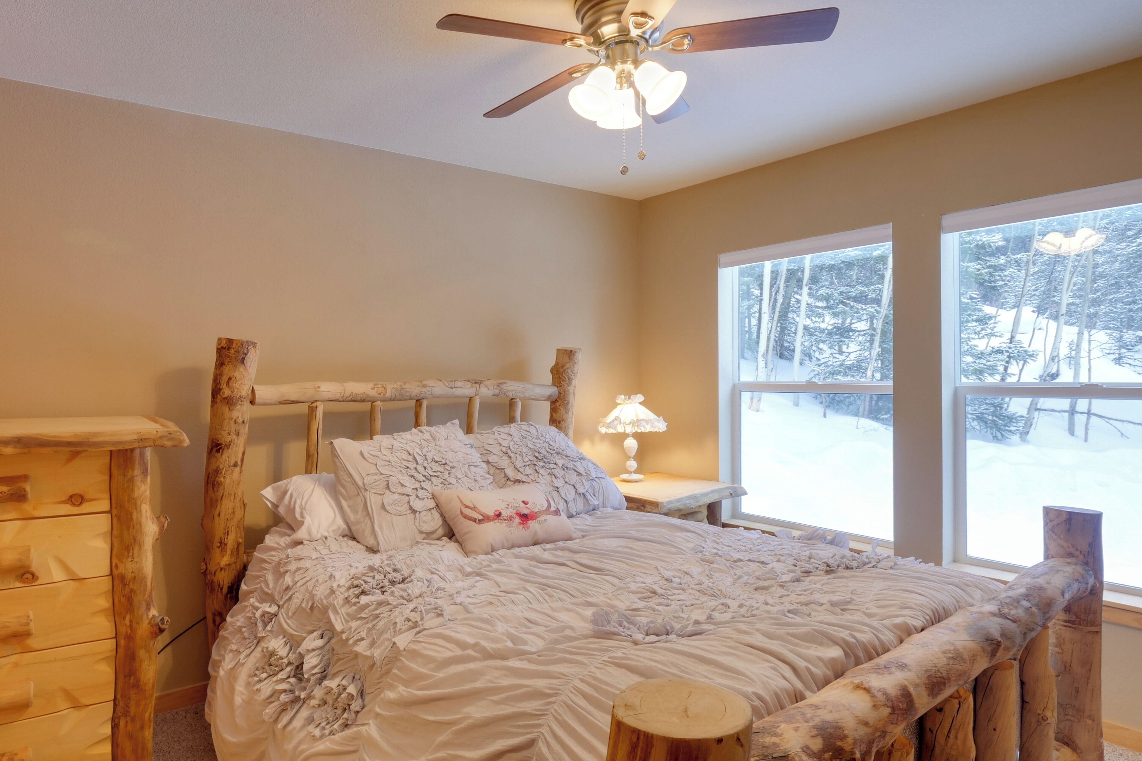 A cozy bedroom with a wooden headboard, a large window with a snowy view, and a ceiling fan.
