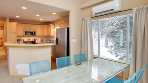 A modern kitchen with a central island, a dining area with a glass table, and a view of snow-covered trees through a large window.