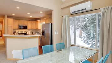 A modern kitchen with a central island, a dining area with a glass table, and a view of snow-covered trees through a large window.