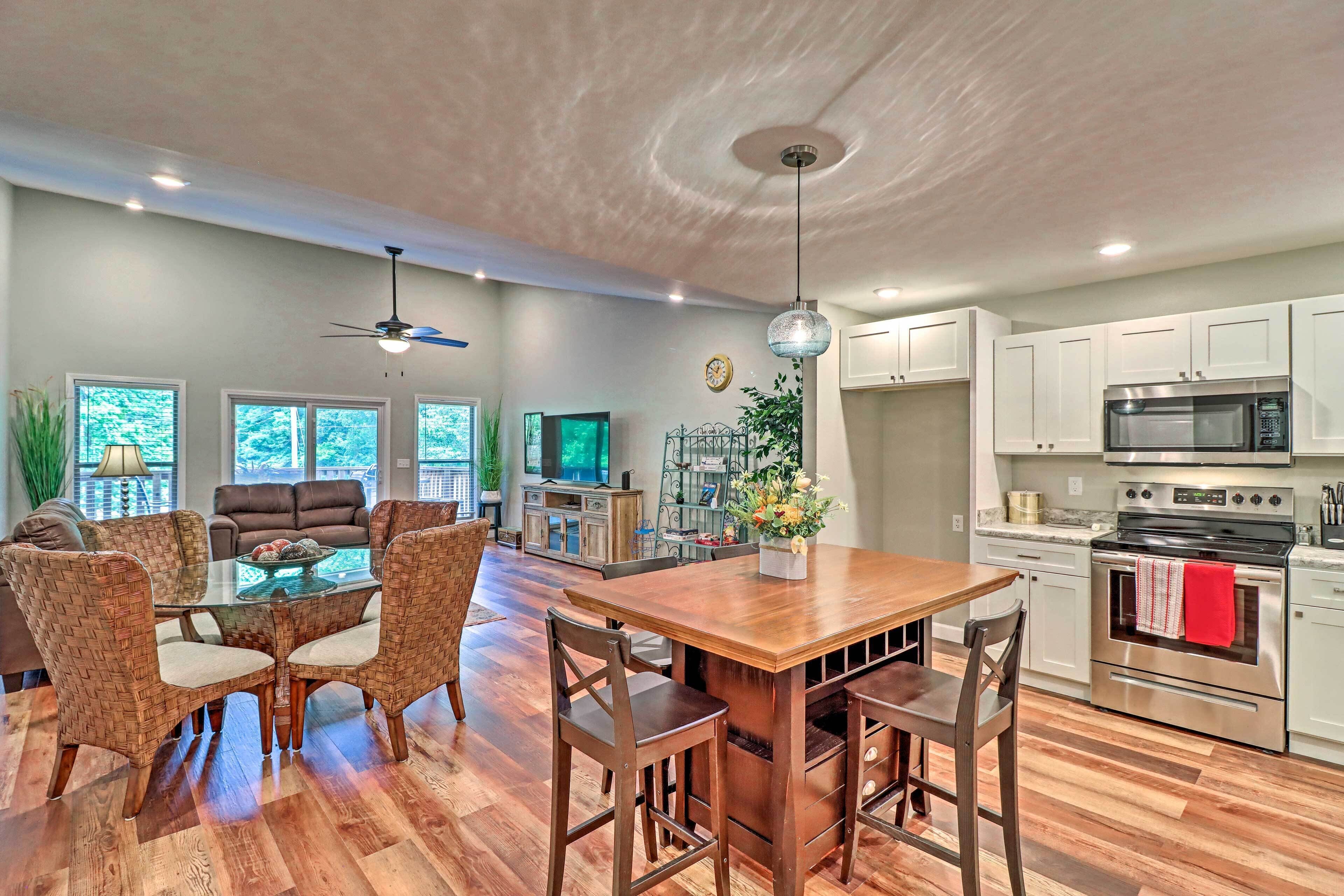 A spacious living room with a wooden dining table, comfortable seating, a television, and a kitchen area with modern appliances.