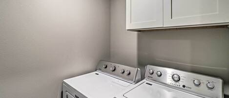 A laundry room with two stacked washers and dryers, white walls, and a cabinet above.