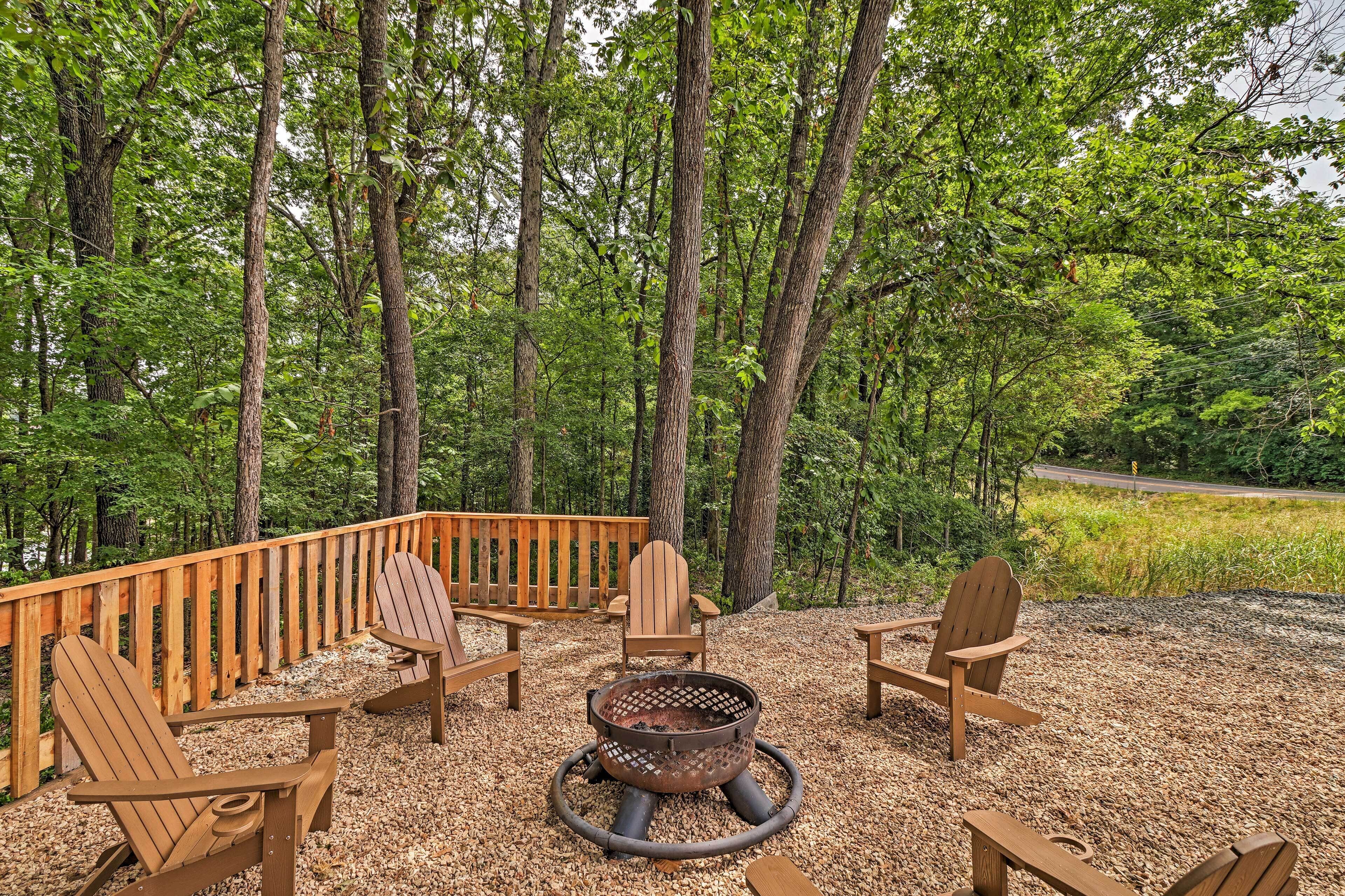 A deck with Adirondack chairs and a fire pit surrounded by a forest.