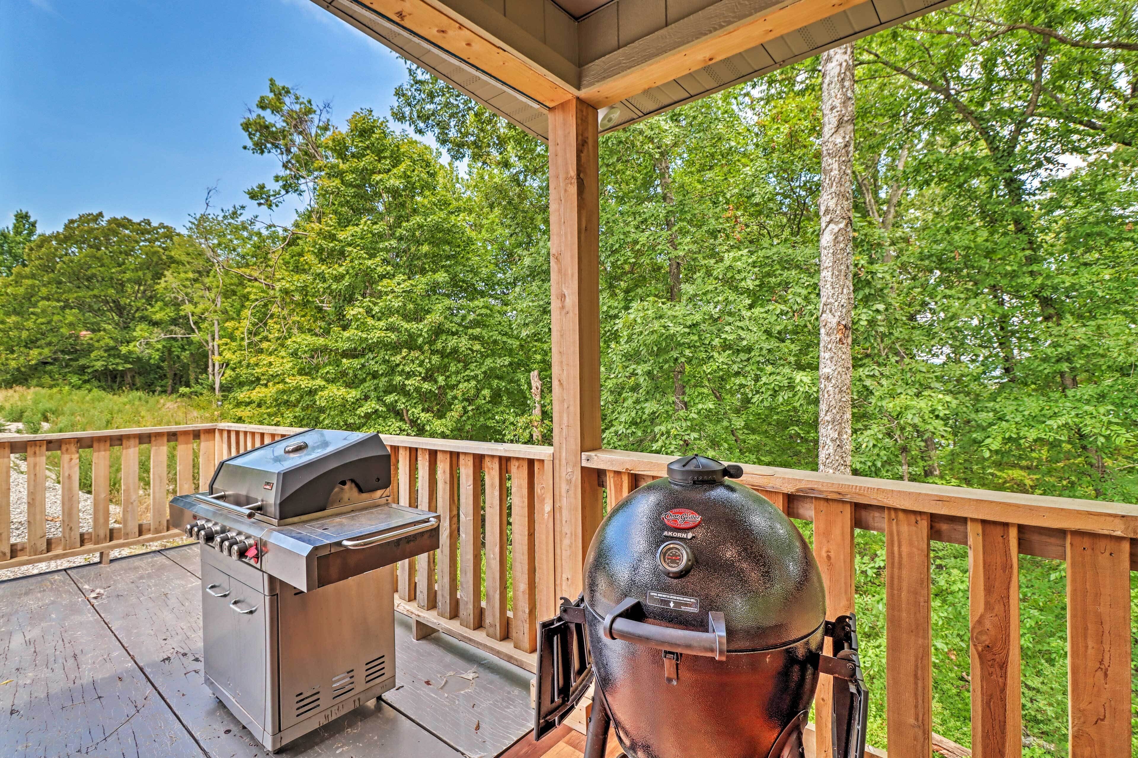 Un barbecue et un fumoir sont installés sur une terrasse extérieure dotée d’une rambarde en bois, le tout entouré d’une végétation luxuriante.