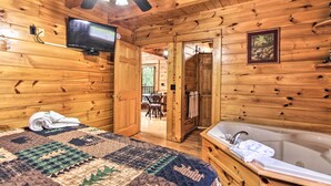 Een houten kamer met een bed, een aan de muur bevestigde televisie, een badkamer met een bad en een deur naar een eetgedeelte.