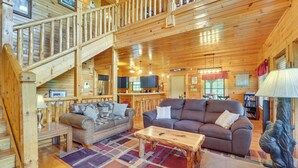 A wooden cabin interior with a staircase, two sofas, a coffee table, and a dining area.