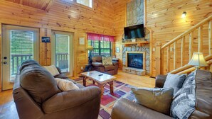 A wooden cabin interior with a fireplace, a television, and a staircase.