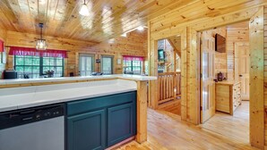 A wooden cabin interior with a kitchen area, wooden walls, and a dining area.