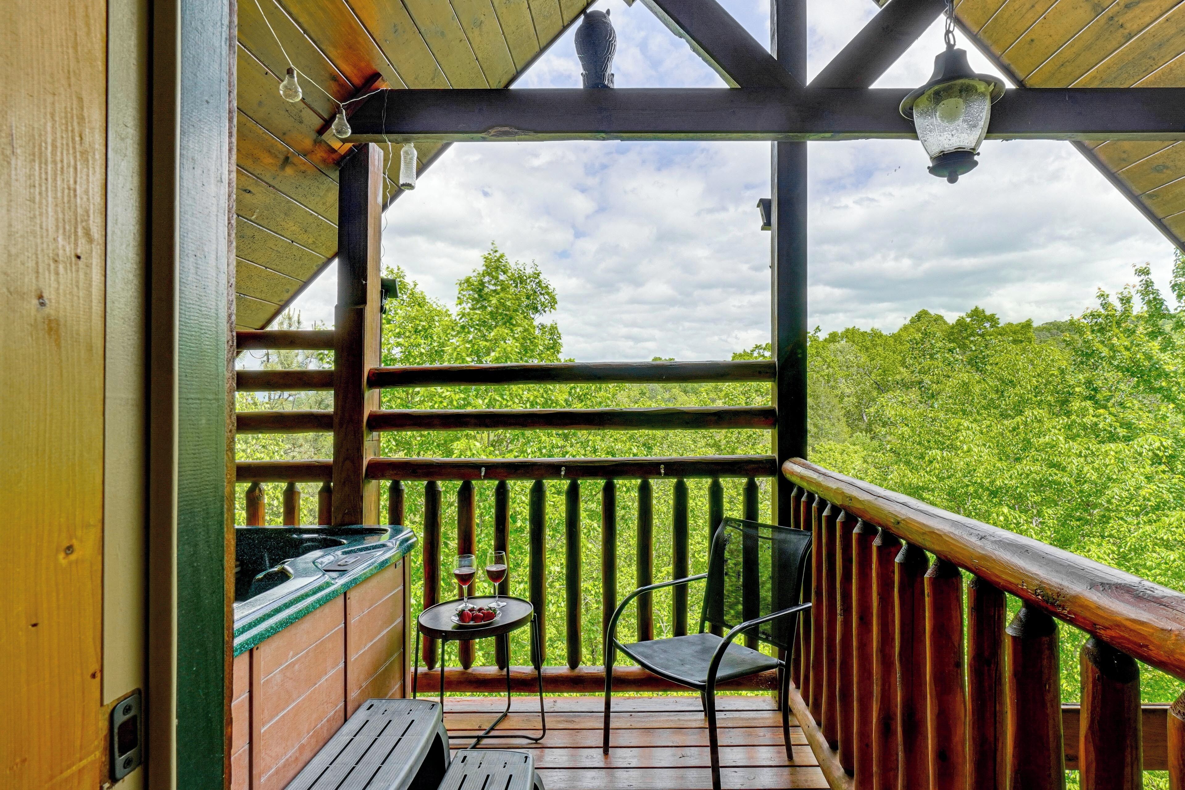 A wooden deck with a view of a green landscape, a table with two glasses of red wine, and a chair.