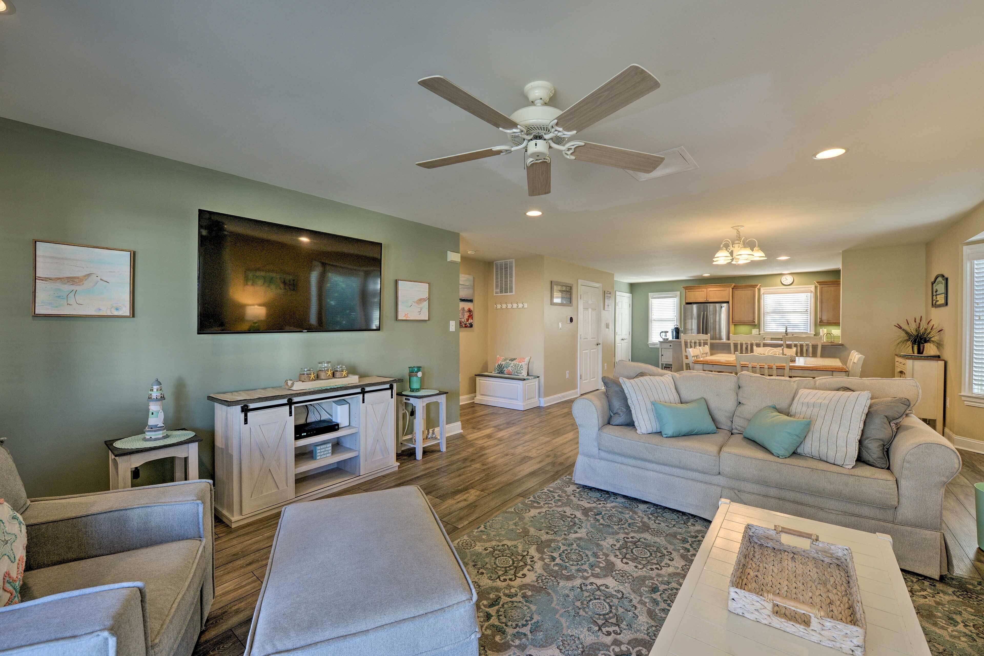 A spacious living room with a large TV, a ceiling fan, and a dining area in the background.