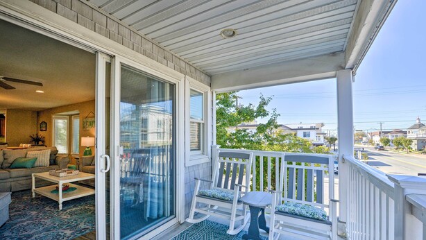 A covered porch with a sliding glass door leading to a living room, a small table, and two rocking chairs. - Wildwood Townhome w/ Patio: 1 Block To The Beach! (Wildwood)