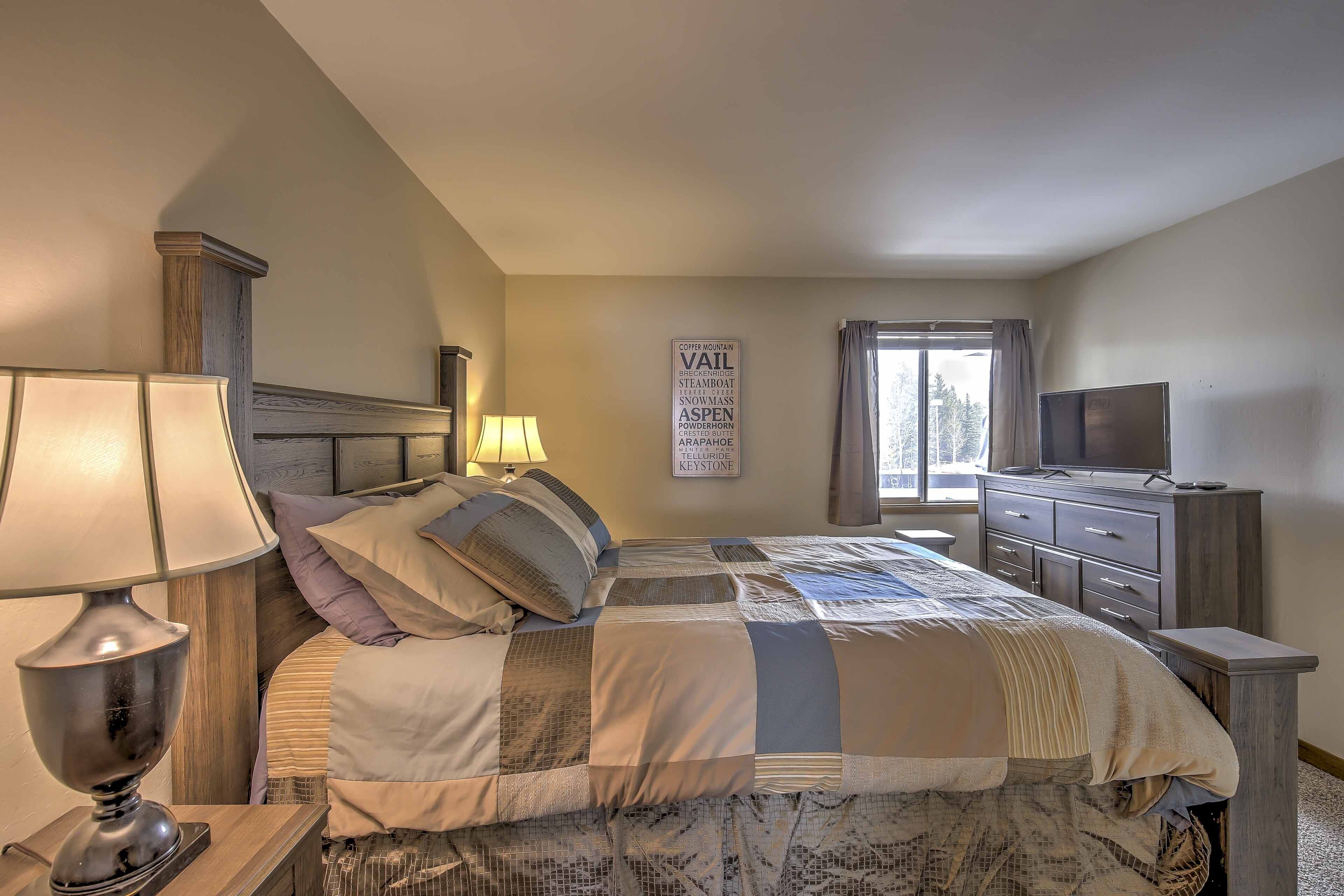 Un dormitorio con cama, lámparas de noche, cómoda, televisor y ventana con cortinas.