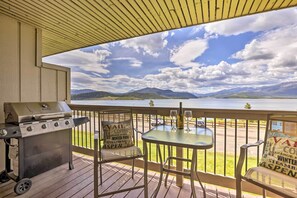 A deck with a grill, a table with two glasses, and a view of mountains and a lake. - Lakefront Dillon Condo w/ Pool Access: Near Skiing (Dillon)