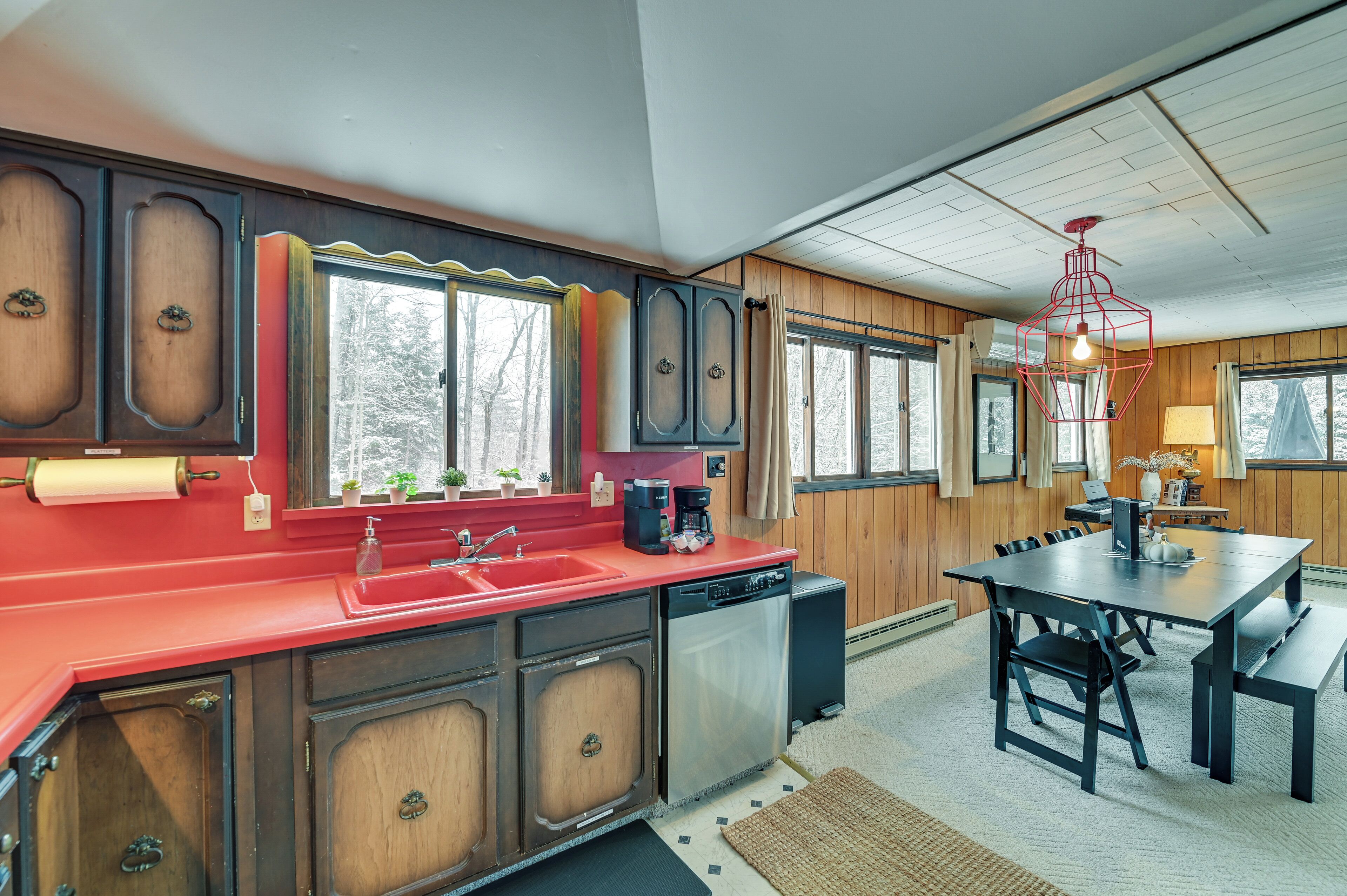 A kitchen with wooden cabinets, a red countertop, and a dishwasher. There is a dining area with a table and chairs.