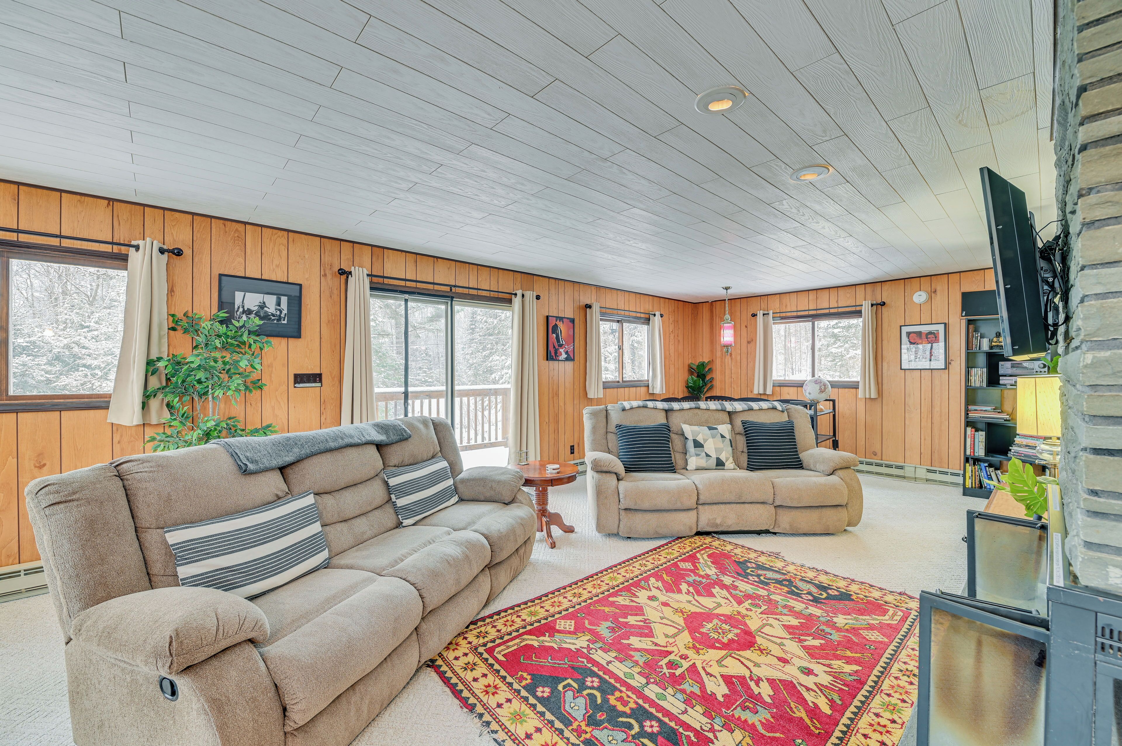 A cozy living room with two sofas, a patterned rug, and wooden paneling.