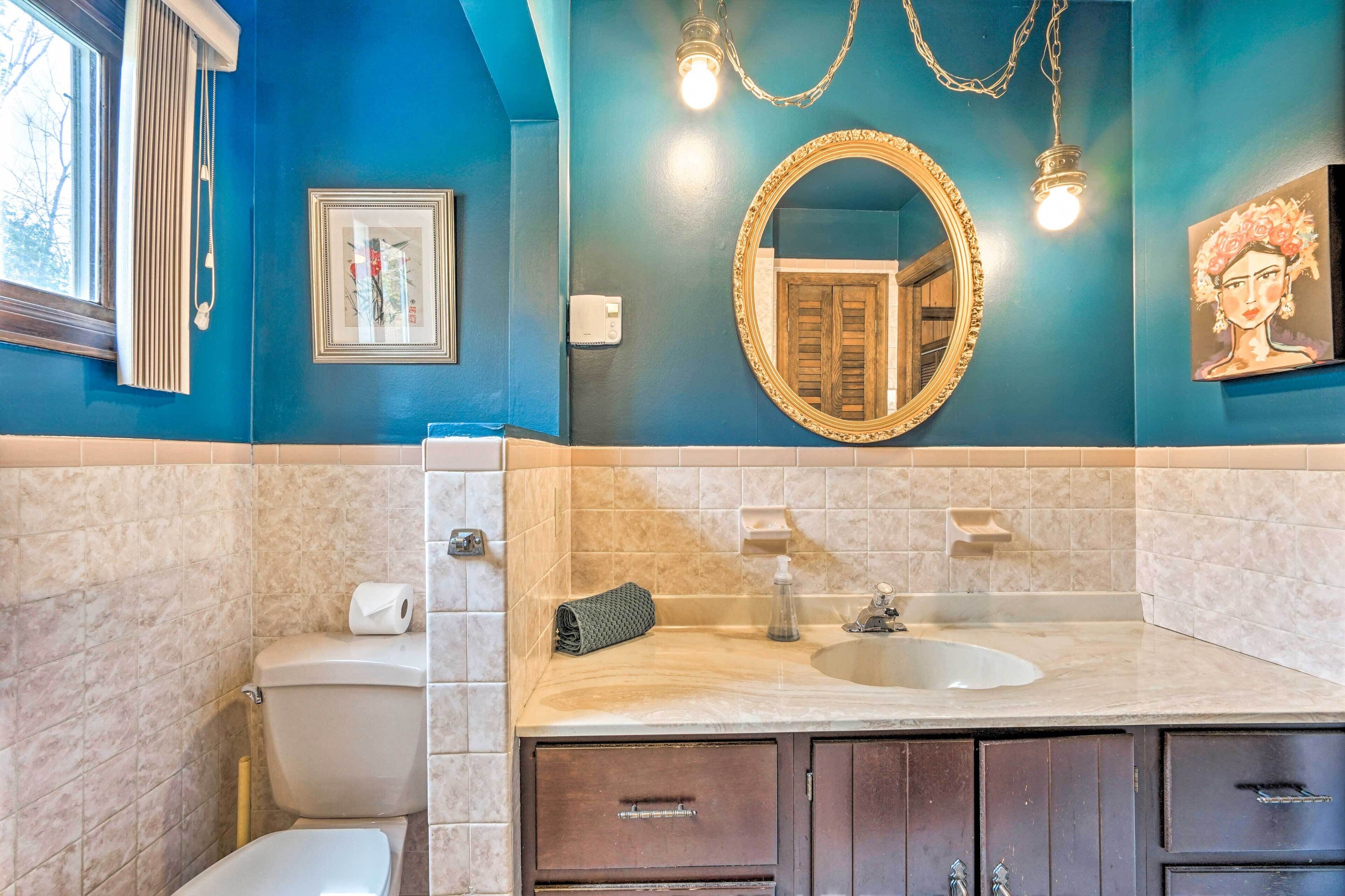 Un baño con pared azul, inodoro blanco, lavabo con espejo y una toalla.