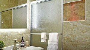 Un bagno con cabina doccia in vetro, lavandino bianco, una bottiglia di sapone e una piccola pianta in vaso.
