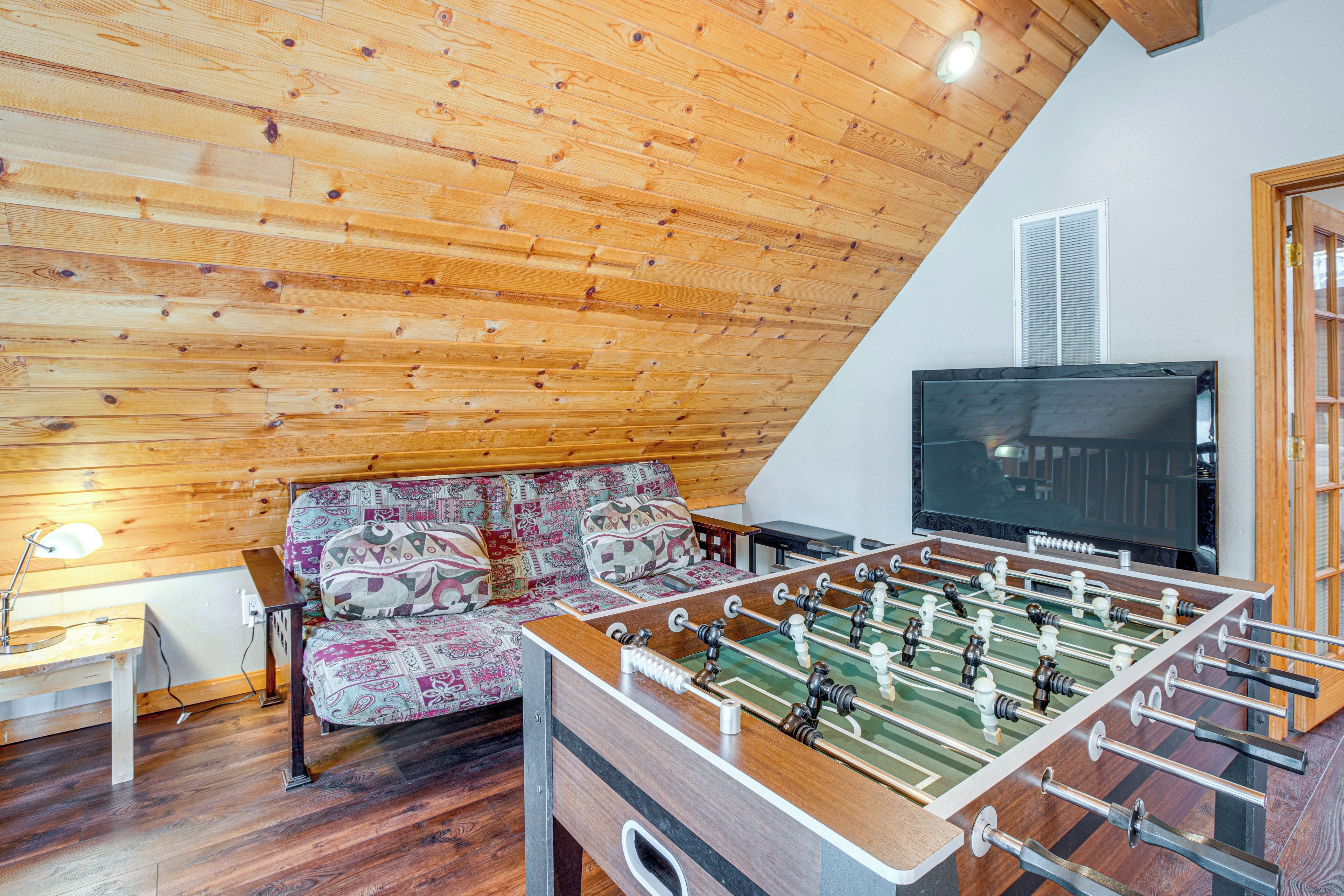 A room with a wooden ceiling, a sofa with patterned cushions, a foosball table, and a television.
