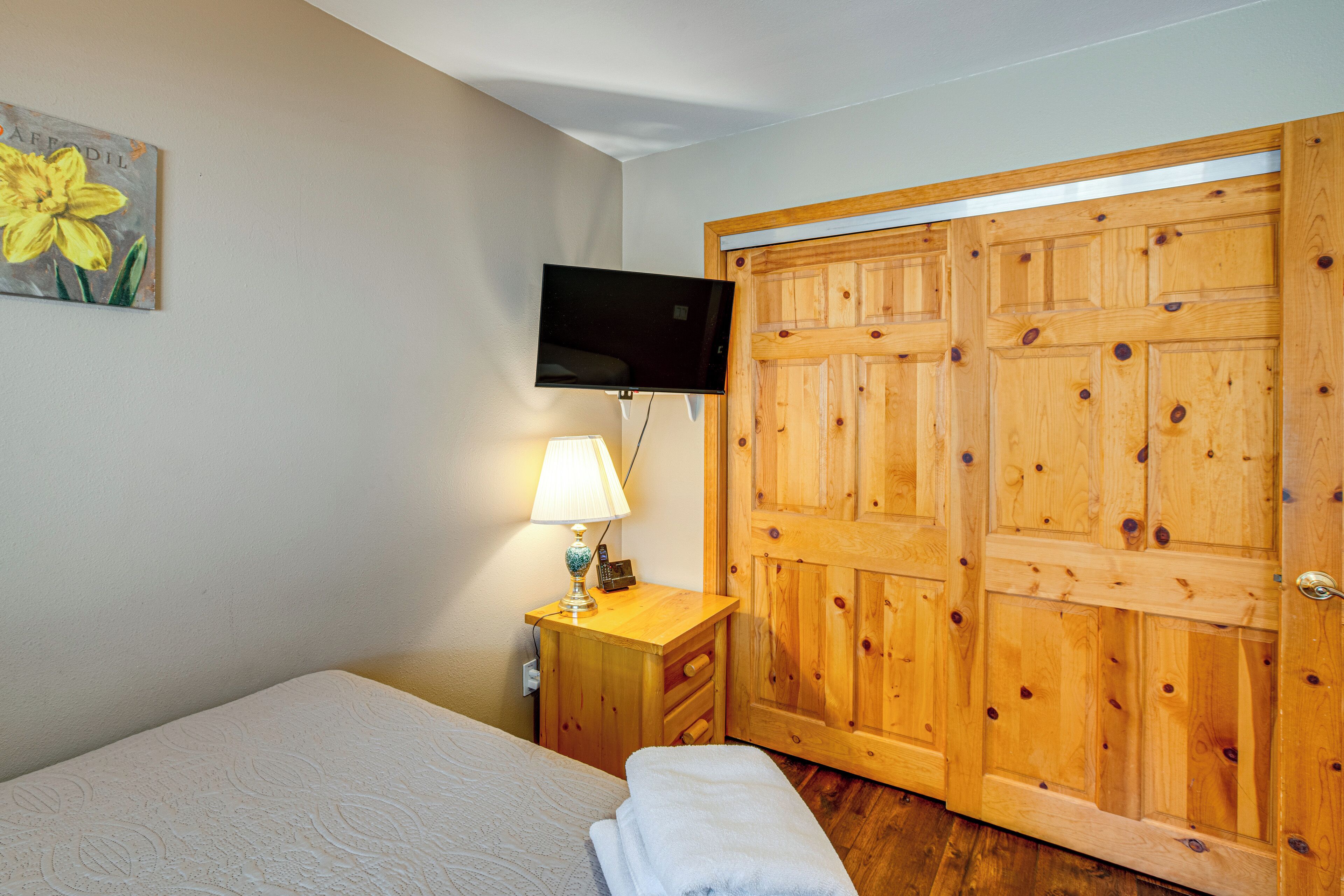 Une chambre à coucher comprenant un lit, une table de chevet avec une lampe, un téléviseur fixé au mur et une armoire en bois.