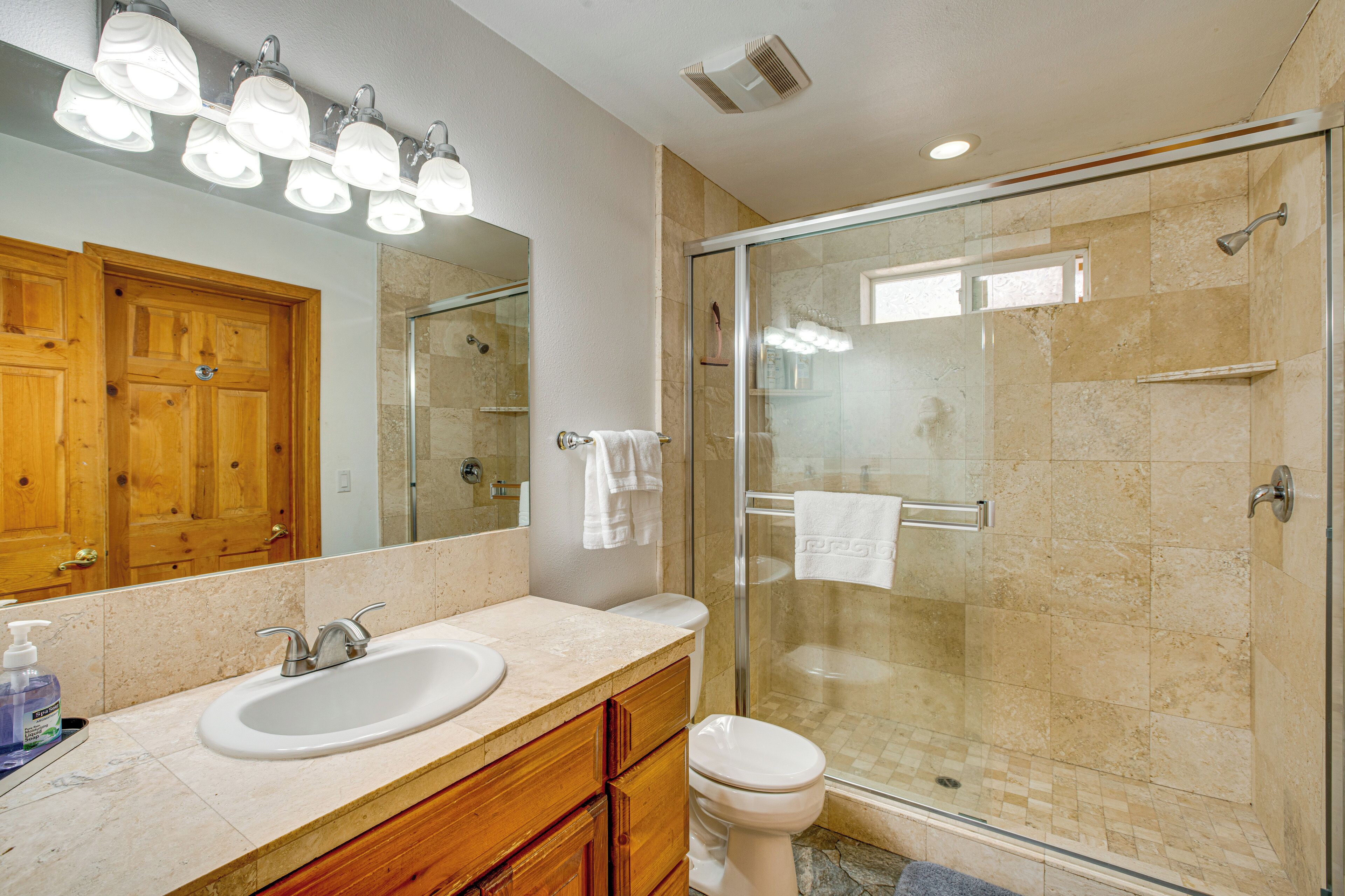 A bathroom with a glass-enclosed shower, a wooden vanity with a sink, and a large mirror.