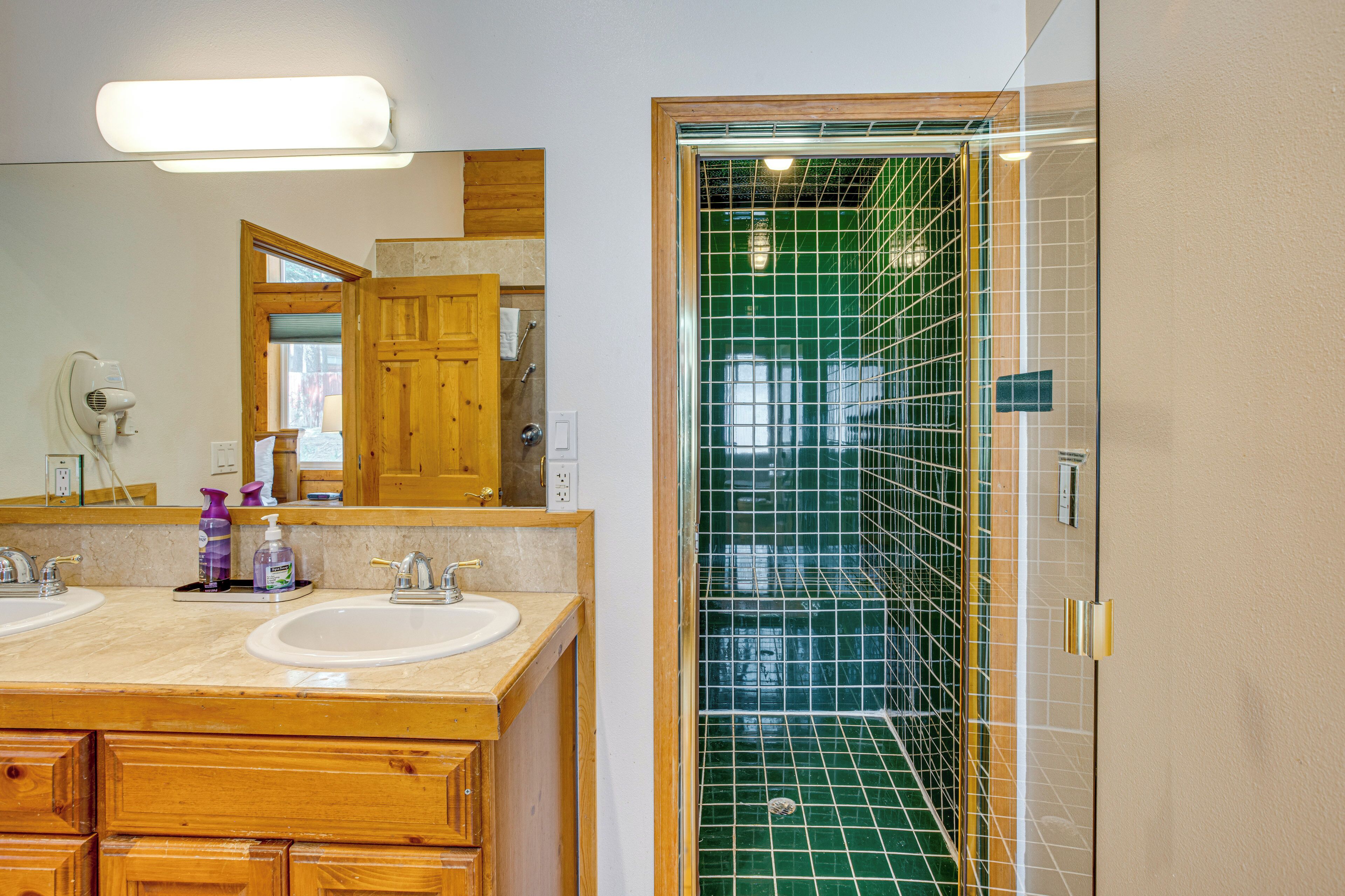 A bathroom with two sinks, a mirror, and a shower with green tiles.