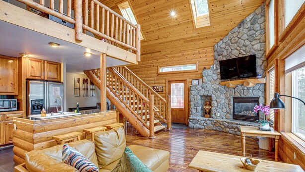 A spacious living area with a wooden staircase, a stone fireplace, and a kitchen with modern appliances.