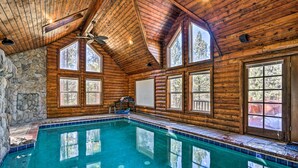 A large indoor swimming pool with wooden walls and stone accents, surrounded by large windows.