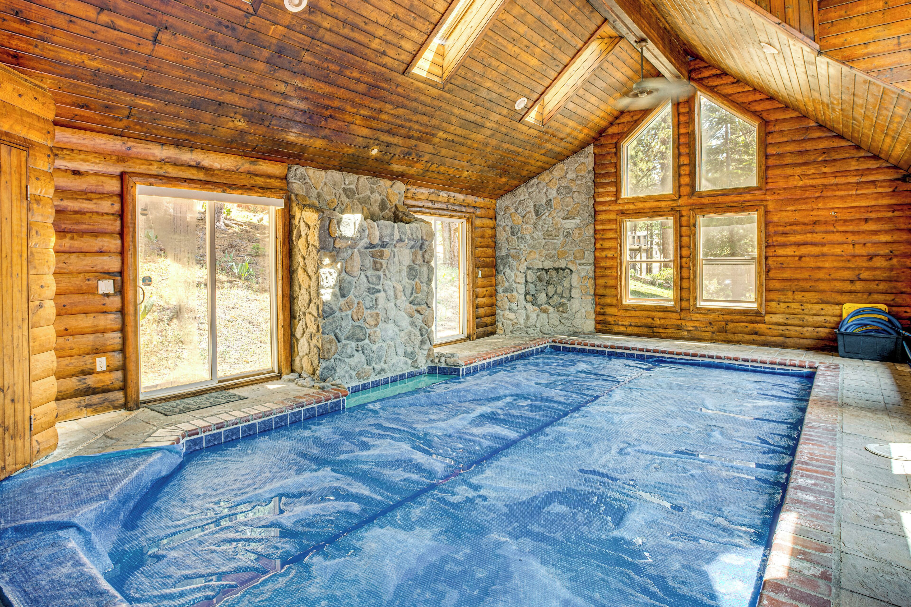 Una cabaña de troncos con pared de piedra, techo de madera y una piscina.