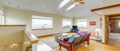 A spacious living room with a wooden floor, a ceiling fan, a sofa, a TV, and large windows.