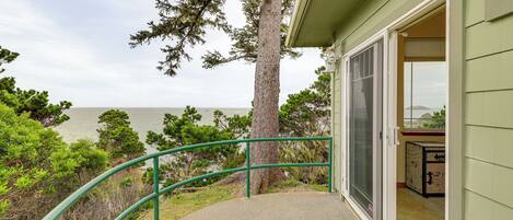 A balcony with a green railing overlooking a body of water, a tree, and a building entrance.