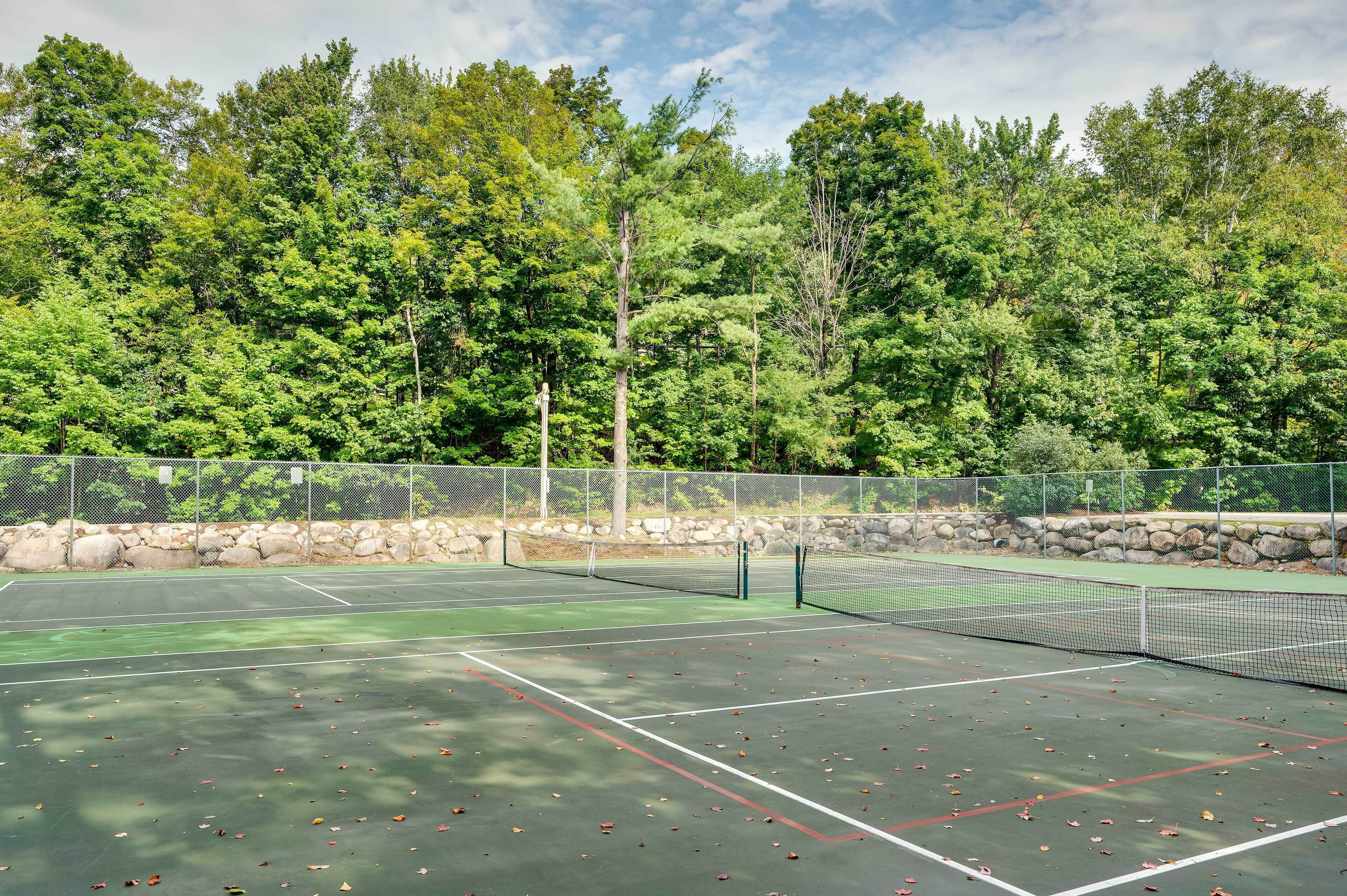An outdoor tennis court surrounded by a stone wall and dense trees.